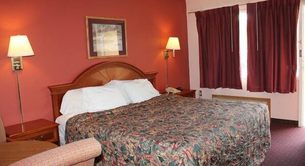 A hotel room with a wooden bed, two bedside lamps, a large window with curtains, and a framed picture on the wall.