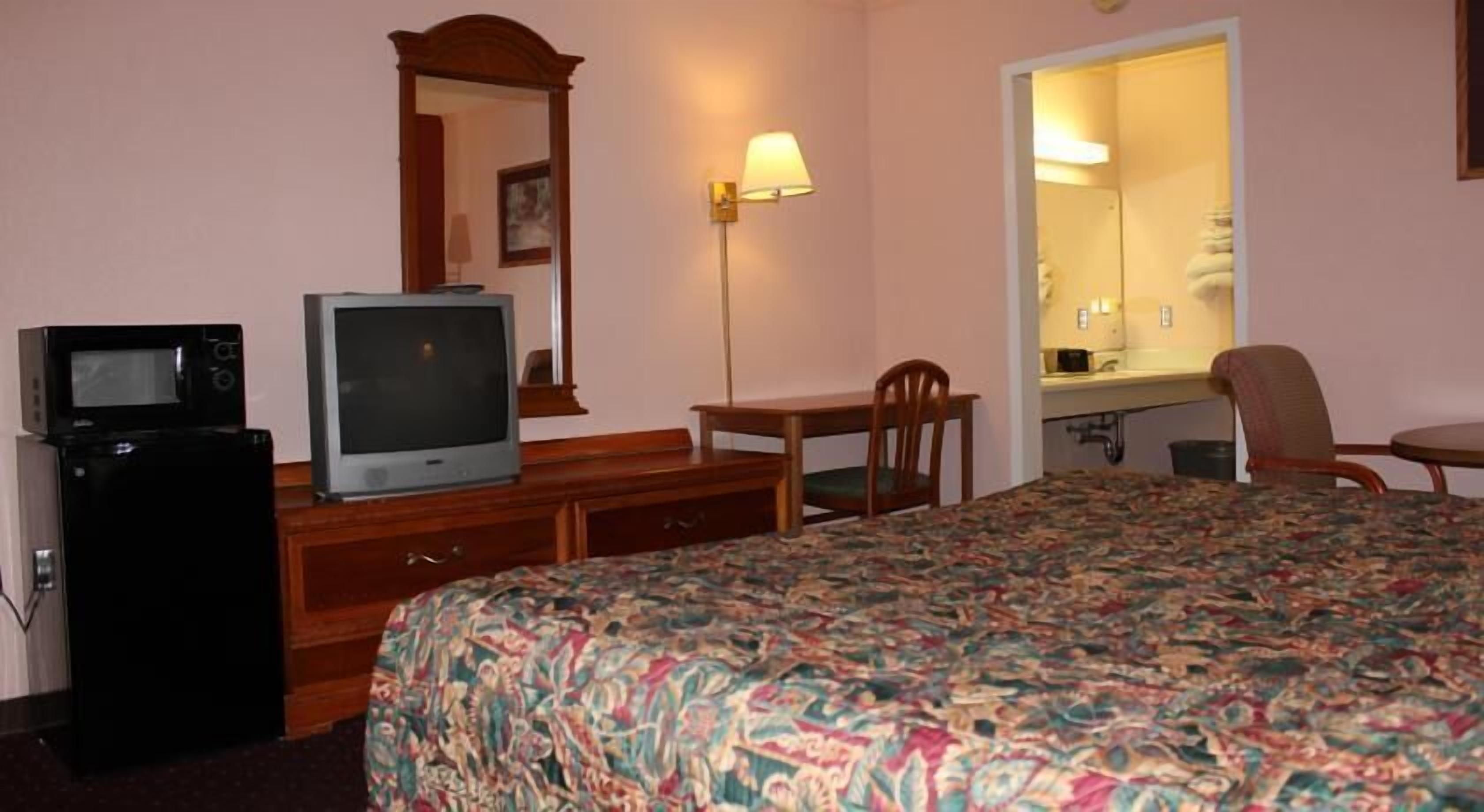 A hotel room with a bed, a desk, a chair, a television, a lamp, and a mirror.
