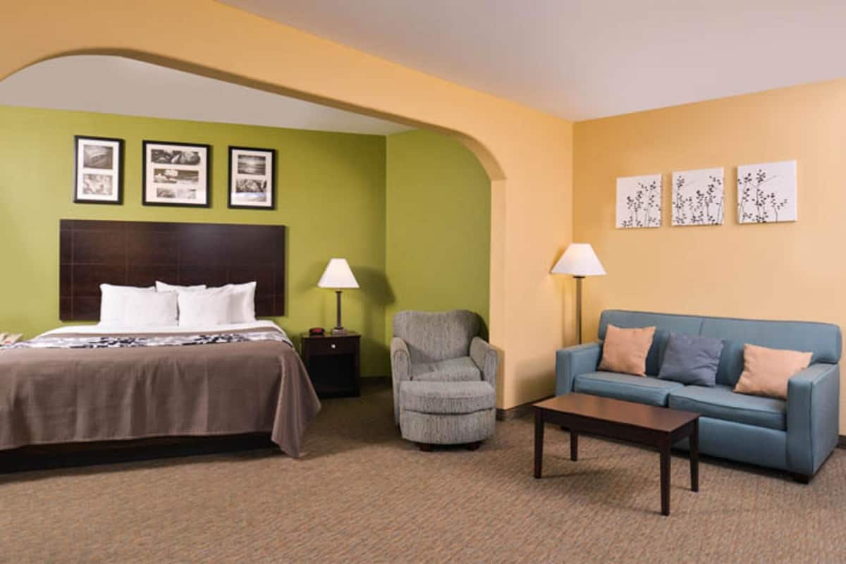 A hotel room with a bed, a sofa, a chair, a coffee table, and framed pictures on the walls.