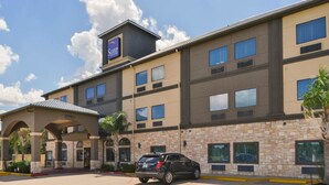A hotel with a stone facade, multiple windows, and a parking lot with a black car.