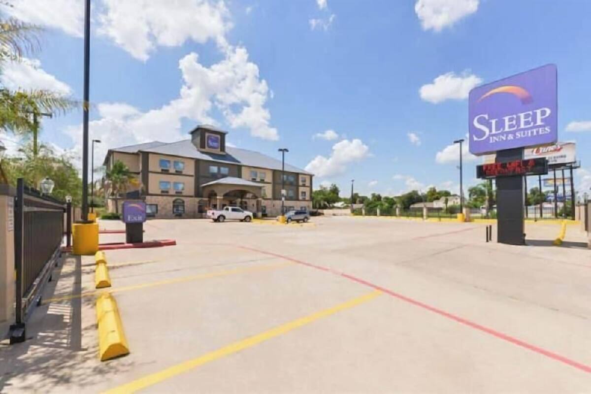 A Sleep Inn & Suites with a parking lot, a building with a flat roof, and a clear blue sky.
