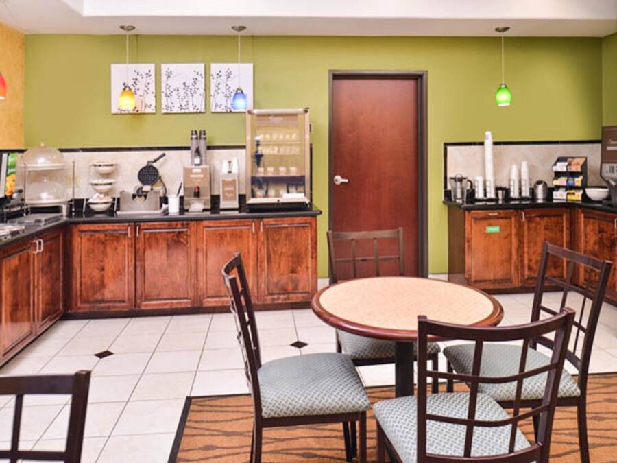 A compact kitchen with wooden cabinets, a round dining table with chairs, and a green wall with artwork.