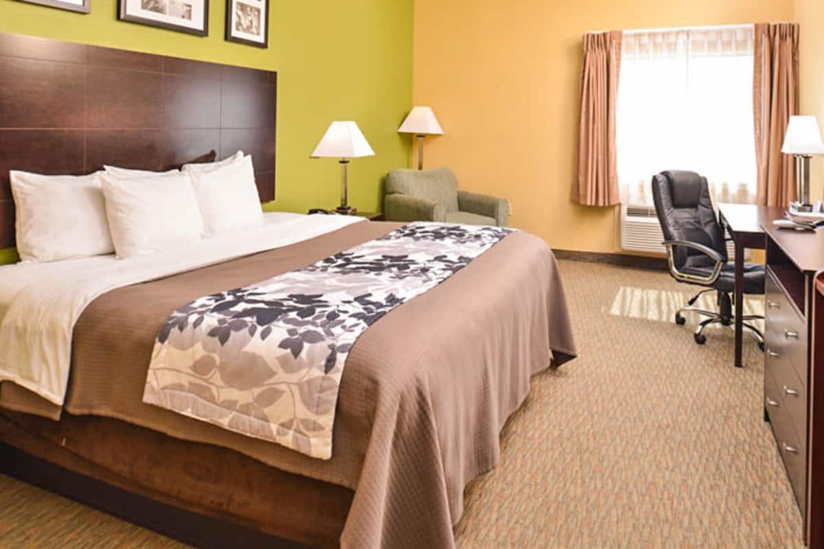 A hotel room with a large bed, two bedside lamps, a desk with a chair, and a window with curtains.