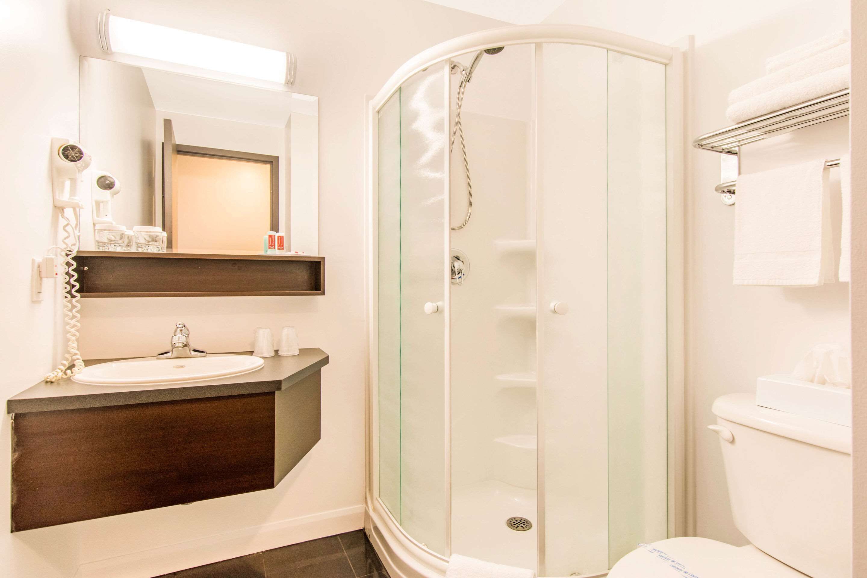 Ein modernes Badezimmer mit einer gläsernen Duschkabine, einem Waschbecken mit dunkler Arbeitsplatte und einem Spiegel darüber.