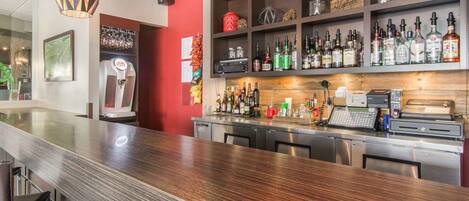 Una zona de bar con mostrador de madera pulida, diversos botelleros y una caja registradora.