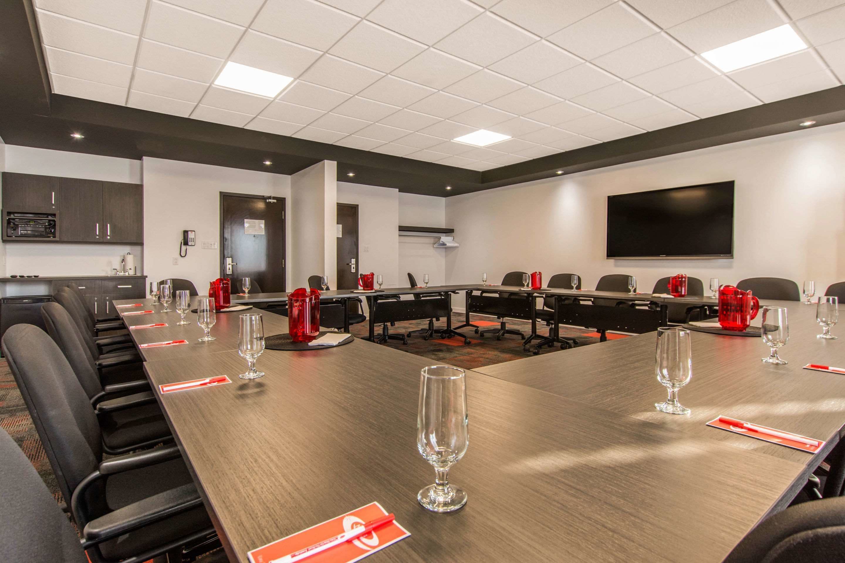 Un salón de conferencias con una larga mesa, sillas y un televisor de pantalla plana en la pared.