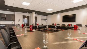 Un salón de conferencias con una larga mesa, sillas y un televisor de pantalla plana en la pared.