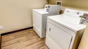A laundry room with two stacked washers and dryers, wooden flooring, and a white wall.