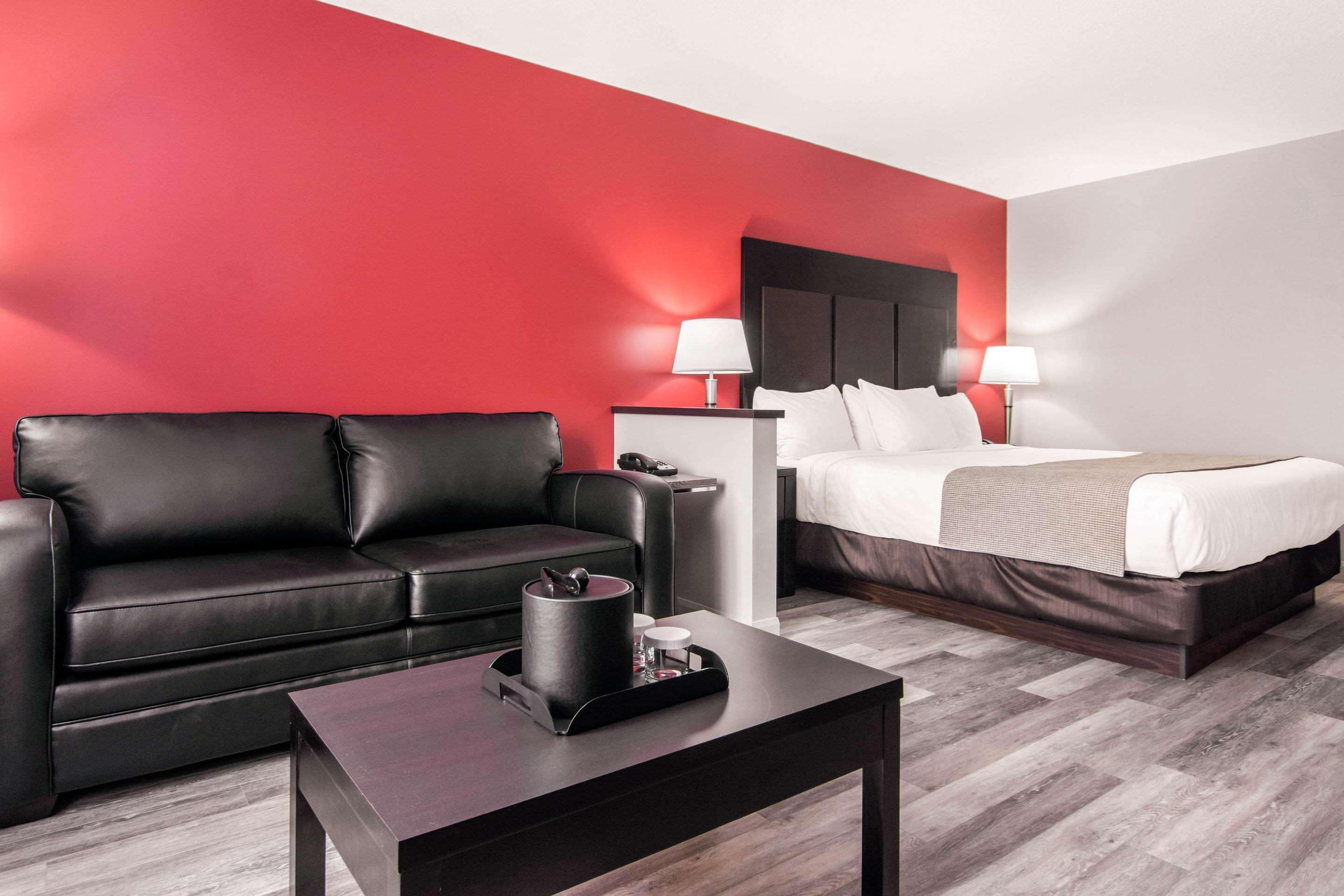 A modern hotel room with a black leather sofa, a bed with white linens, a small table with a tray, and a red accent wall.