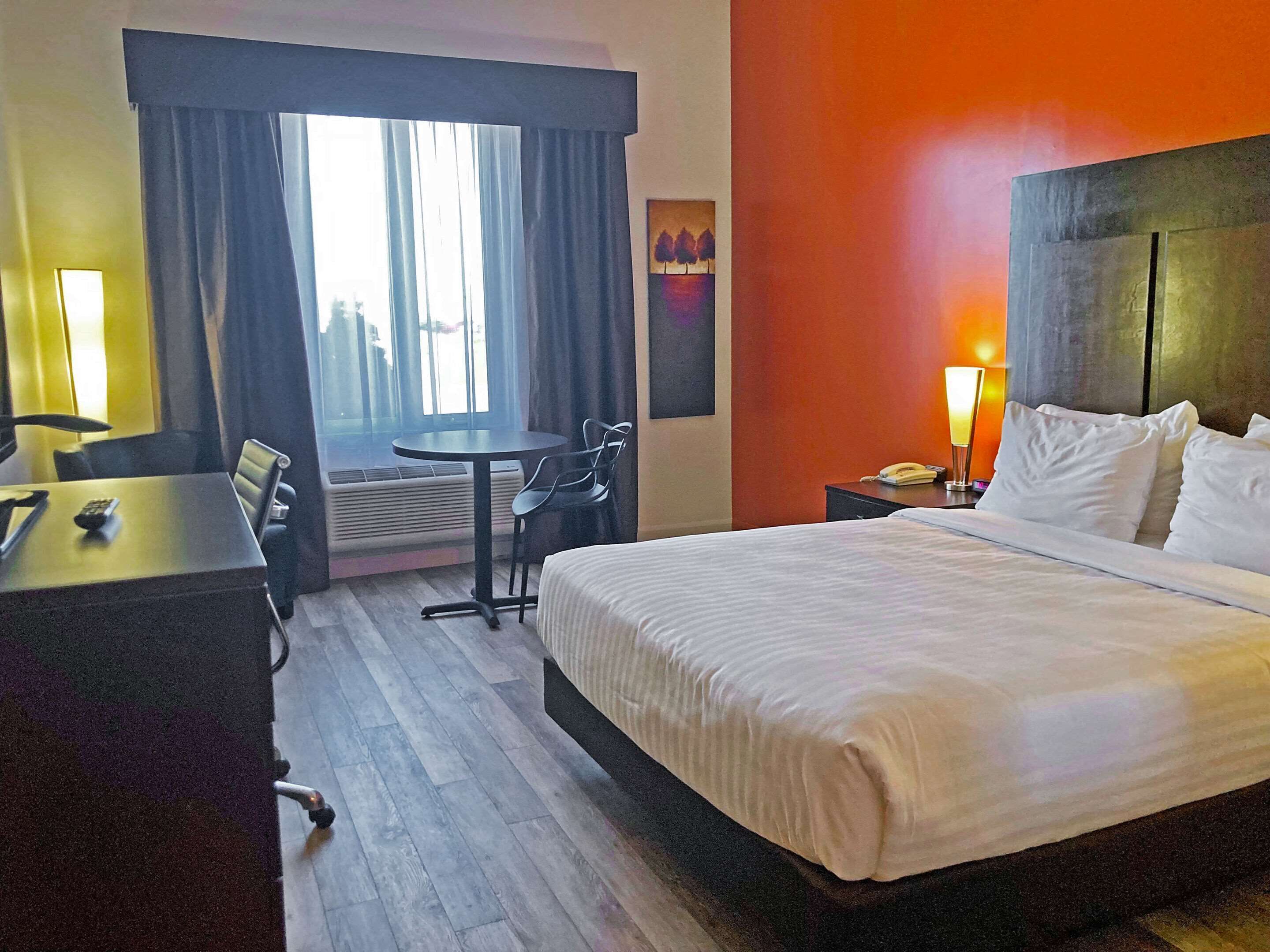 A hotel room with a bed, a desk, a chair, a small table, and a window with curtains.