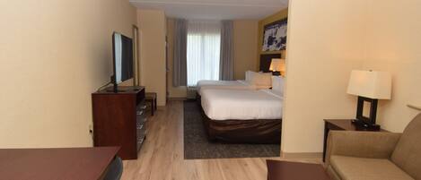 Habitación de hotel con cama, escritorio, silla, sofá, televisor y ventana con cortinas.