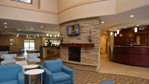 A lobby with blue armchairs, a fireplace, a TV mounted on a stone wall, and a reception desk.