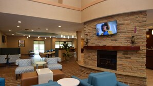 A spacious lobby with a fireplace, comfortable seating, and a television mounted on a brick wall.