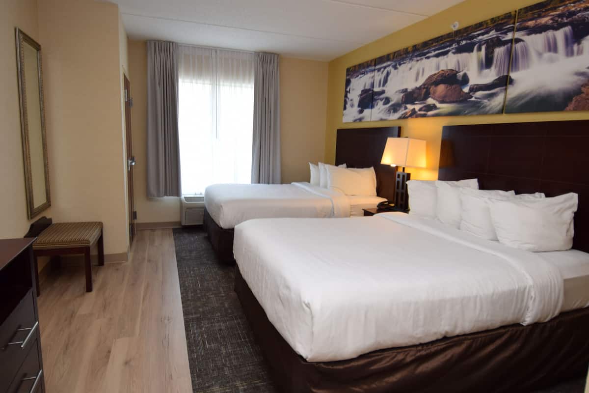 Een hotelkamer met twee bedden, een bureau, een stoel, een groot raam met gordijnen en een schilderij van een waterval aan de muur.