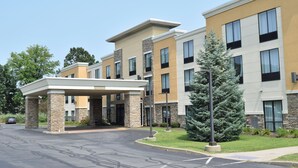 A multi-story hotel with a covered entrance, stone and brick facade, and a parking lot.