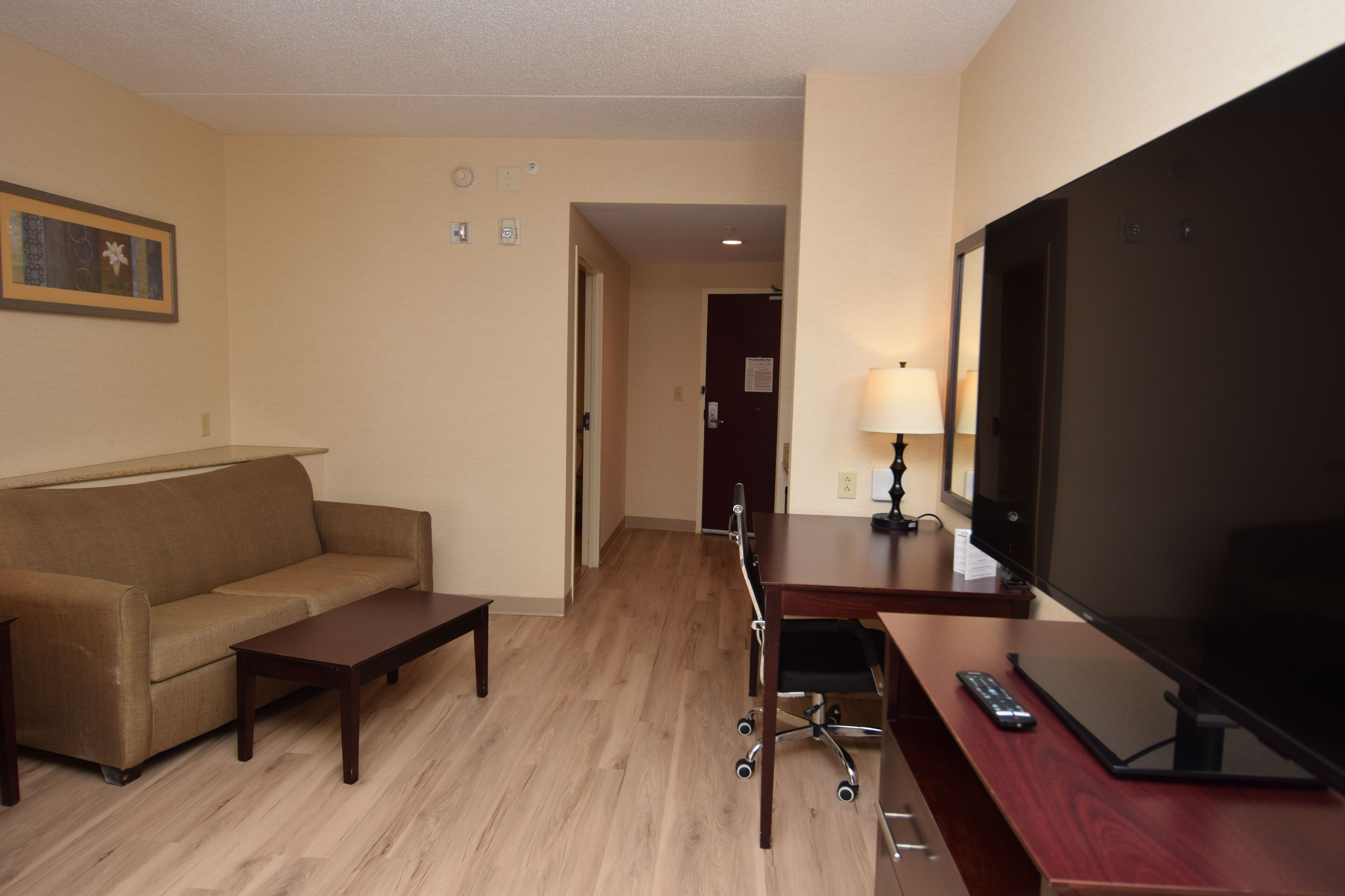 Une chambre d’hôtel équipée d’un canapé, d’un bureau avec un téléviseur à écran plat, d’une lampe et d’une télécommande.