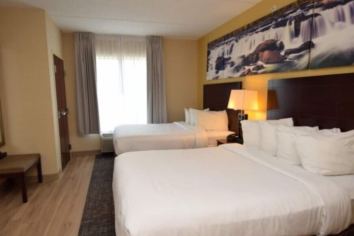Een hotelkamer met twee bedden, een bureau, een stoel, een raam met gordijnen en een schilderij aan de muur.
