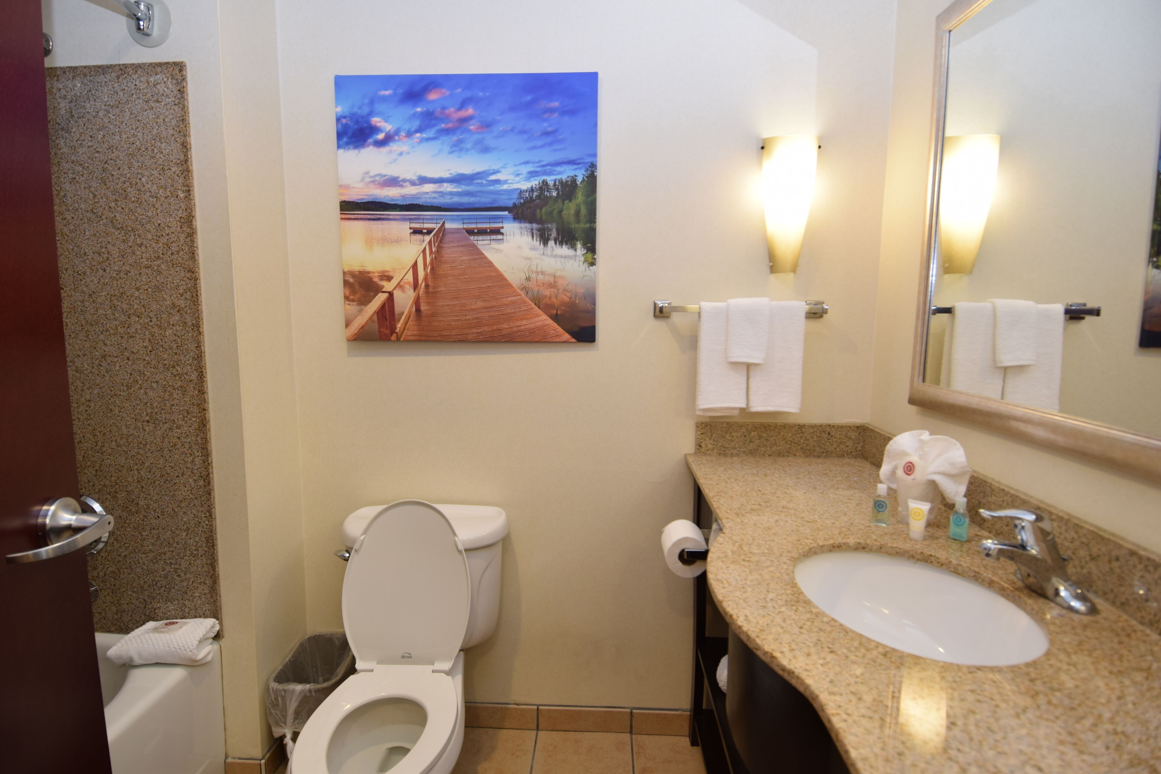 A bathroom with a toilet, sink, and a painting of a dock and lake.