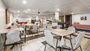 Uma ampla área de jantar com várias mesas e cadeiras, uma cozinha ao fundo e uma toalha quadriculada vermelha e branca sobre uma das mesas.