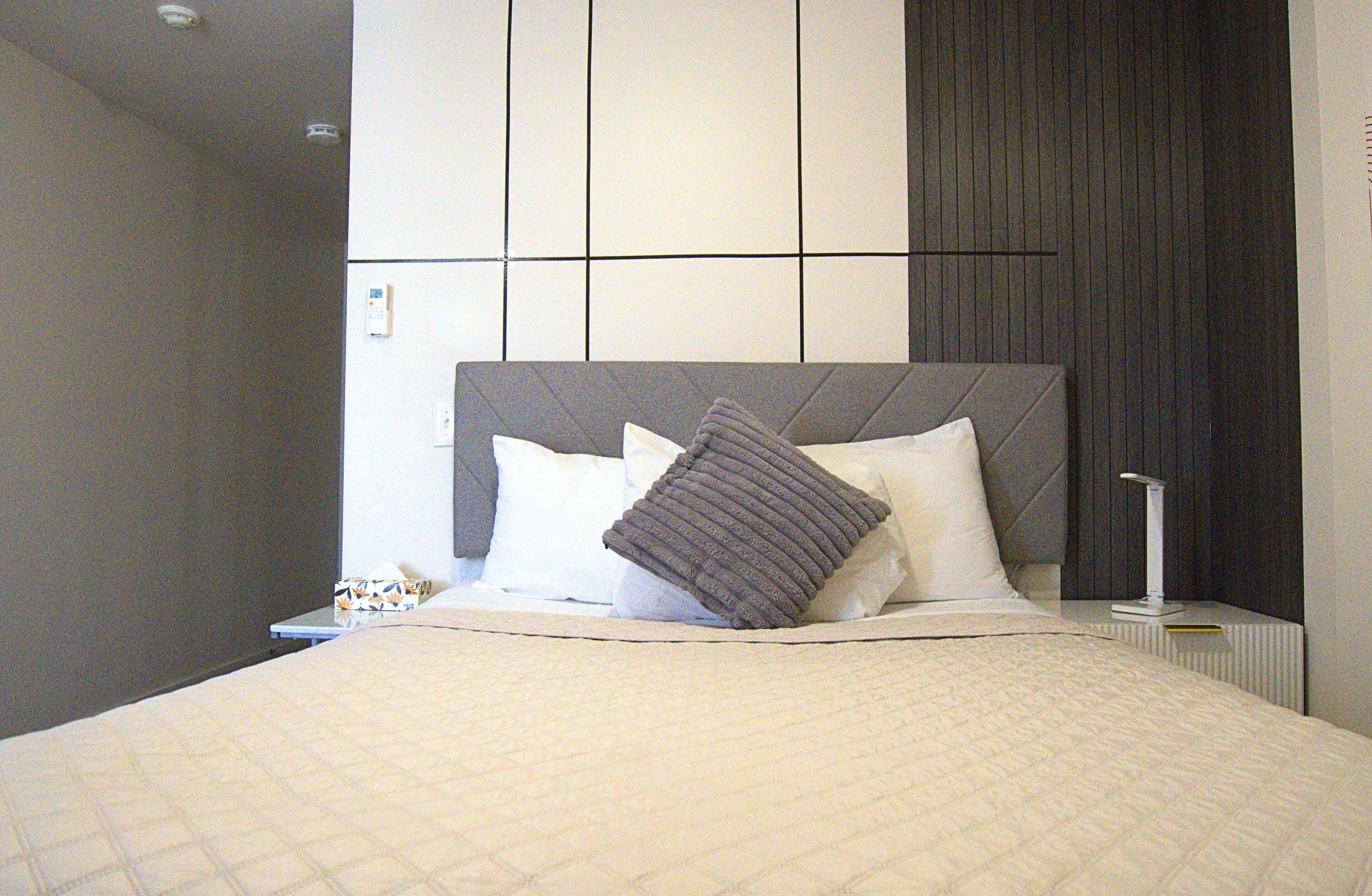 A neatly made bed with a quilted cover, a bedside table with a lamp, and a wall with a panel design.
