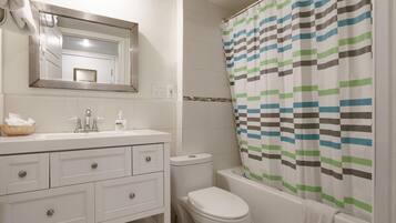A bathroom with a white sink, mirror, and toilet. There is a striped shower curtain and a towel hanging on the bathtub.