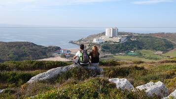 A couple sitting on a rock overlooking a coastal area with a large building in the distance.