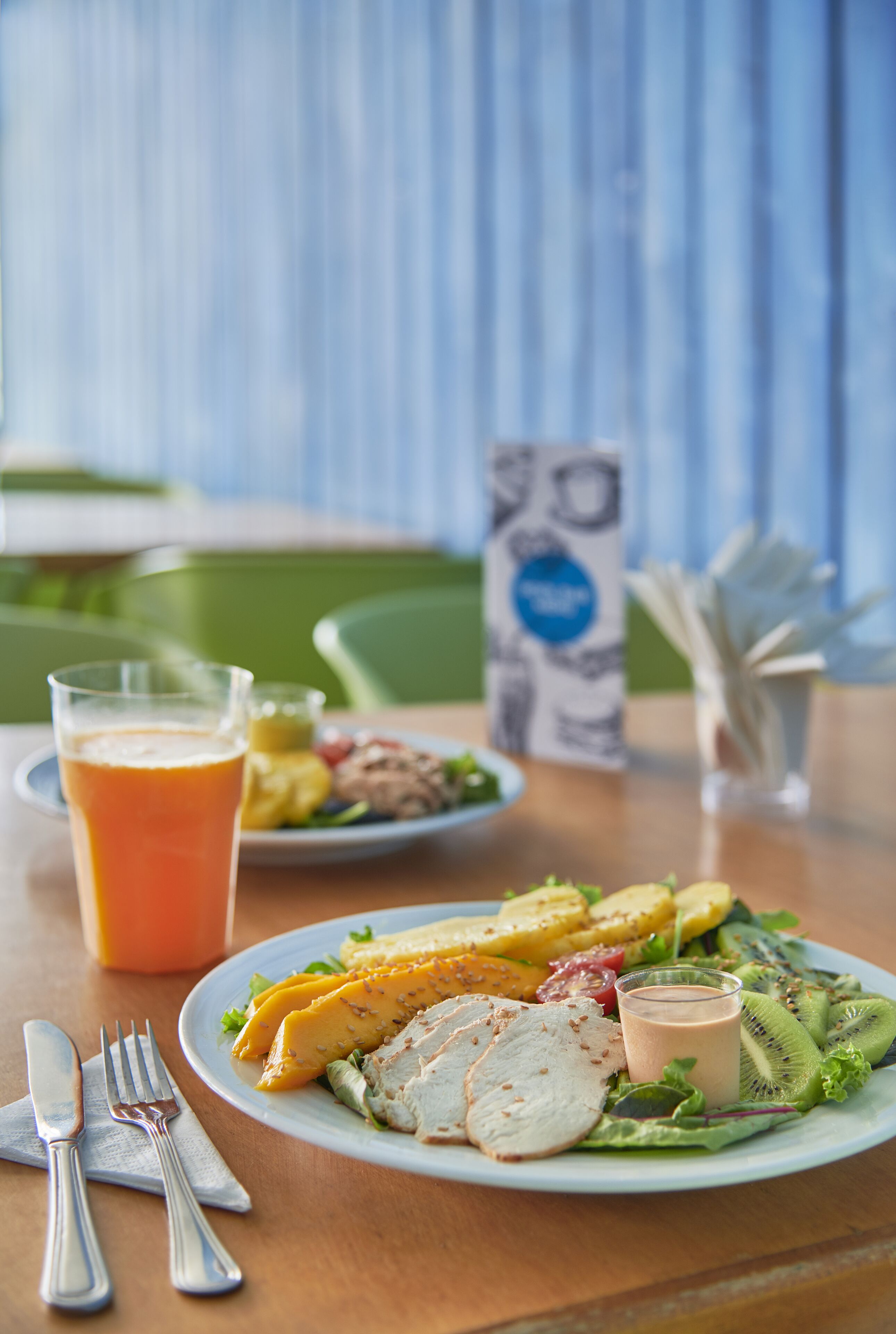 A meal with a glass of orange juice, a plate with sliced meat, vegetables, and a salad, and a menu stand.