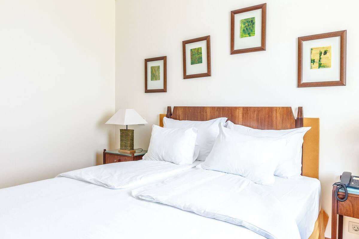 A neatly made bed with white linens, a wooden headboard, and a bedside table with a lamp and a telephone.