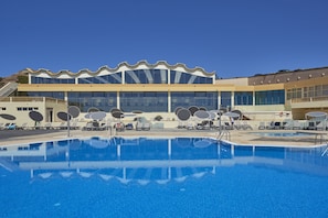 Un hotel moderno con una amplia piscina, tumbonas y un diseño de techo ondulado característico.