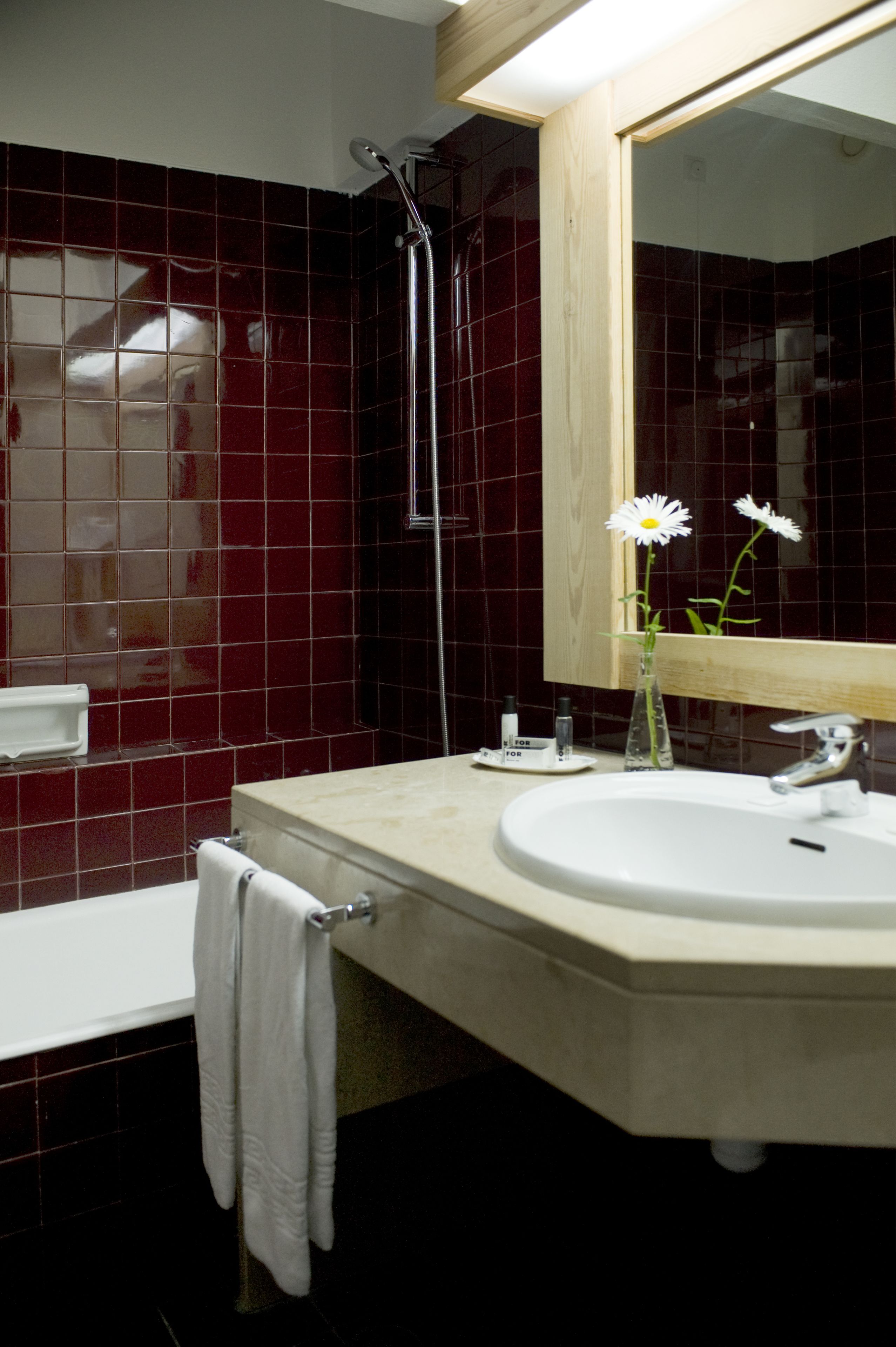 Un baño con lavamanos blanco, un espejo, ducha y pared con azulejos rojos.