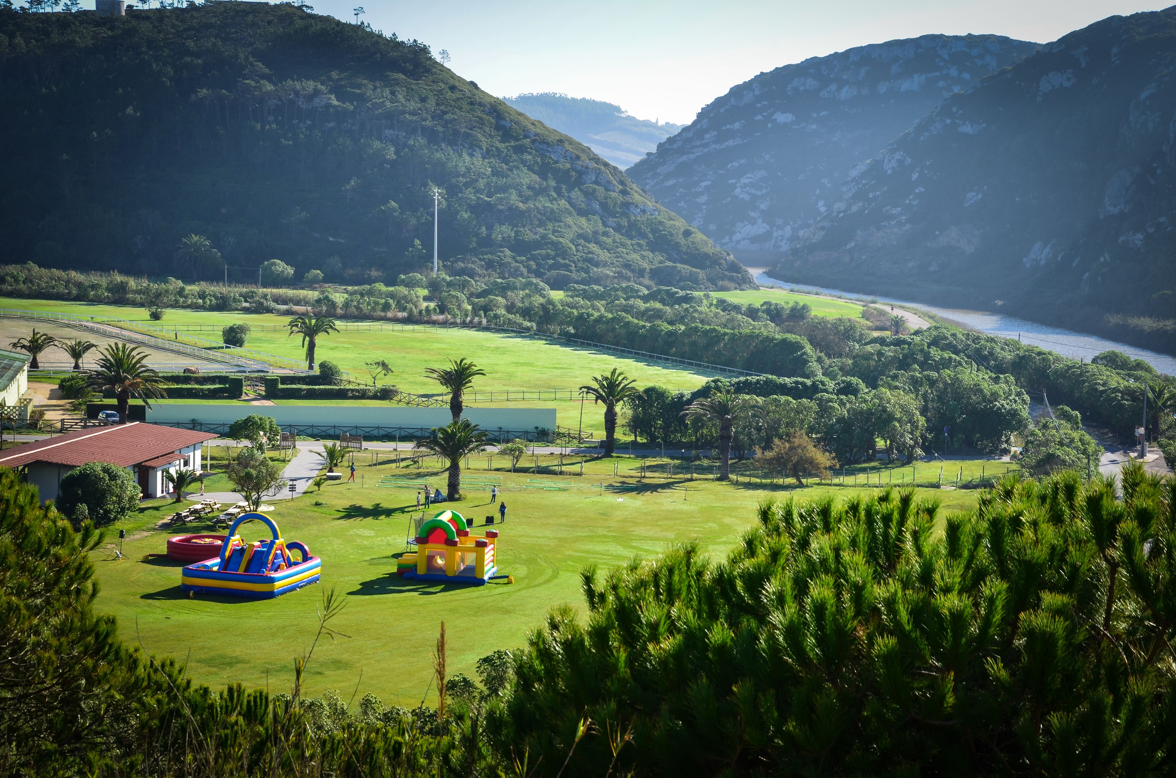 Campo de golf con zona de juegos acuáticos, rodeado de abundante vegetación y montañas.