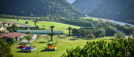 Campo de golf con zona de juegos acuáticos, rodeado de abundante vegetación y montañas.