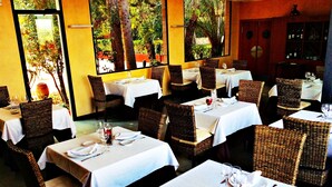 Un restaurante con varias mesas dispuestas para comer, con sillas de mimbre y manteles blancos.
