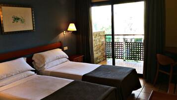 Habitación de hotel con dos camas, una mesita de noche, una lámpara y vistas al balcón exterior.