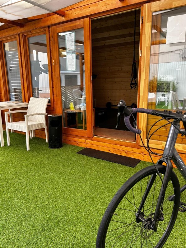 Une cabane en bois avec une porte coulissante en verre, une chaise en osier blanche et un vélo.