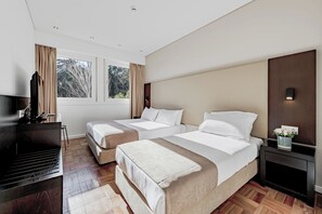 Two single beds with white linens and beige headboards, a desk with a flat-screen TV, and a fireplace.