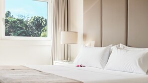 Una cama bien hecha con sábanas blancas, una lámpara de noche y una ventana con vistas a la vegetación.