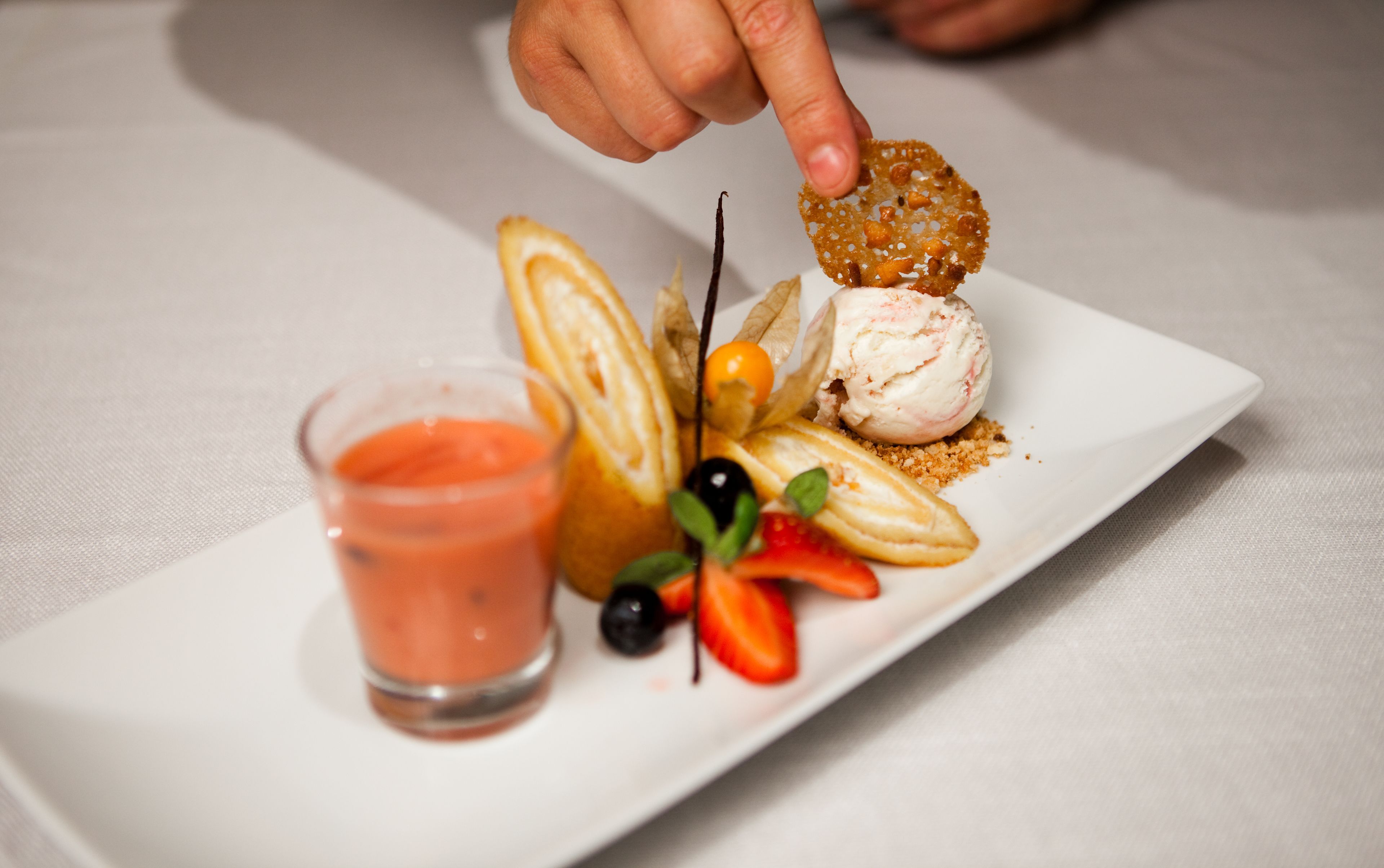 A dessert plate with a scoop of ice cream, a small glass of sauce, and various garnishes.