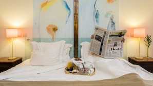 Habitación de hotel con cama, dos lámparas de noche, una bandeja con alimentos para el desayuno y un cuadro en la pared.