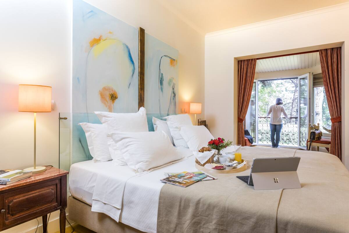 Habitación de hotel con cama, laptop, bandeja con alimentos para el desayuno y ventana con cortinas.