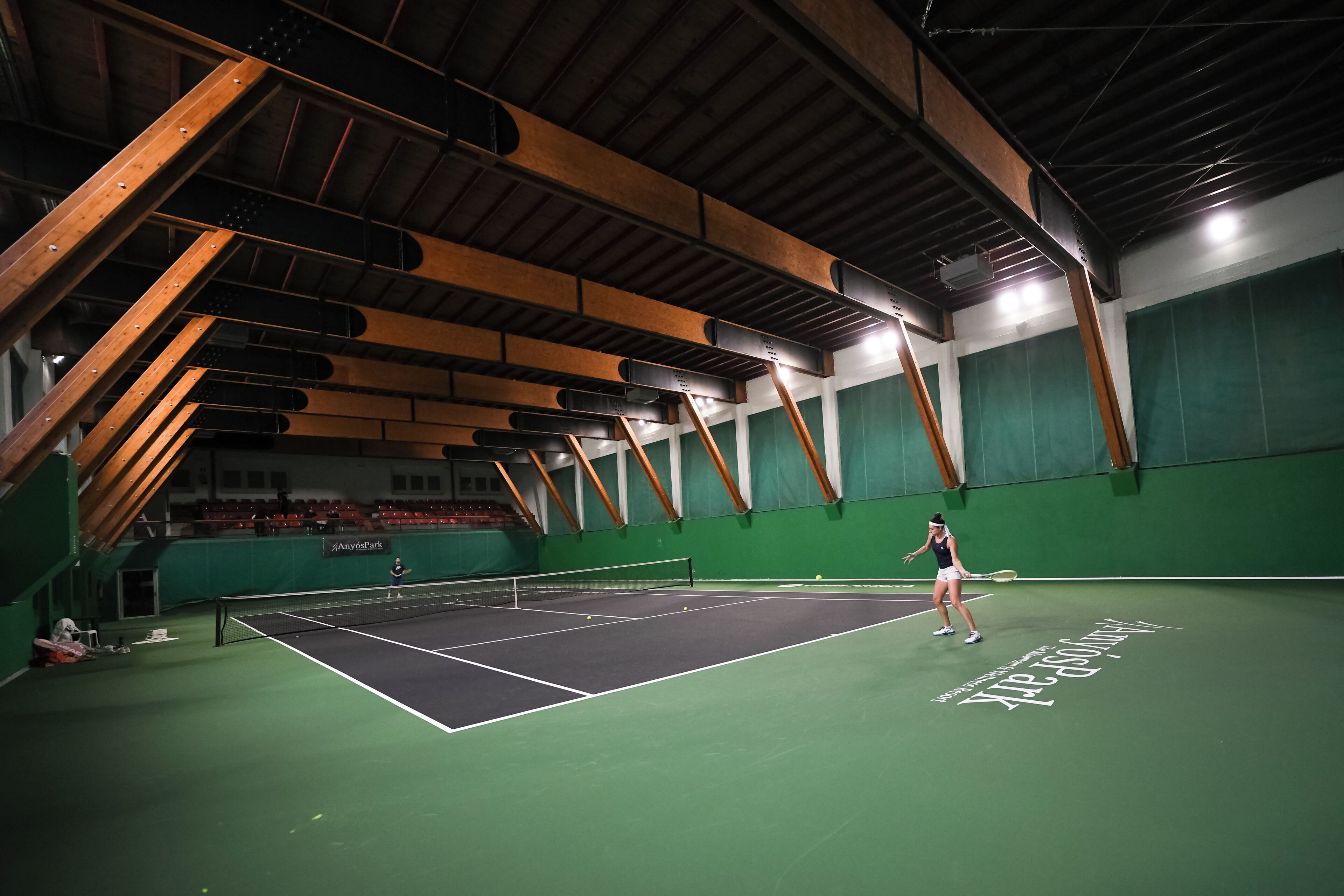 An indoor tennis court with a net, wooden beams, and green walls.