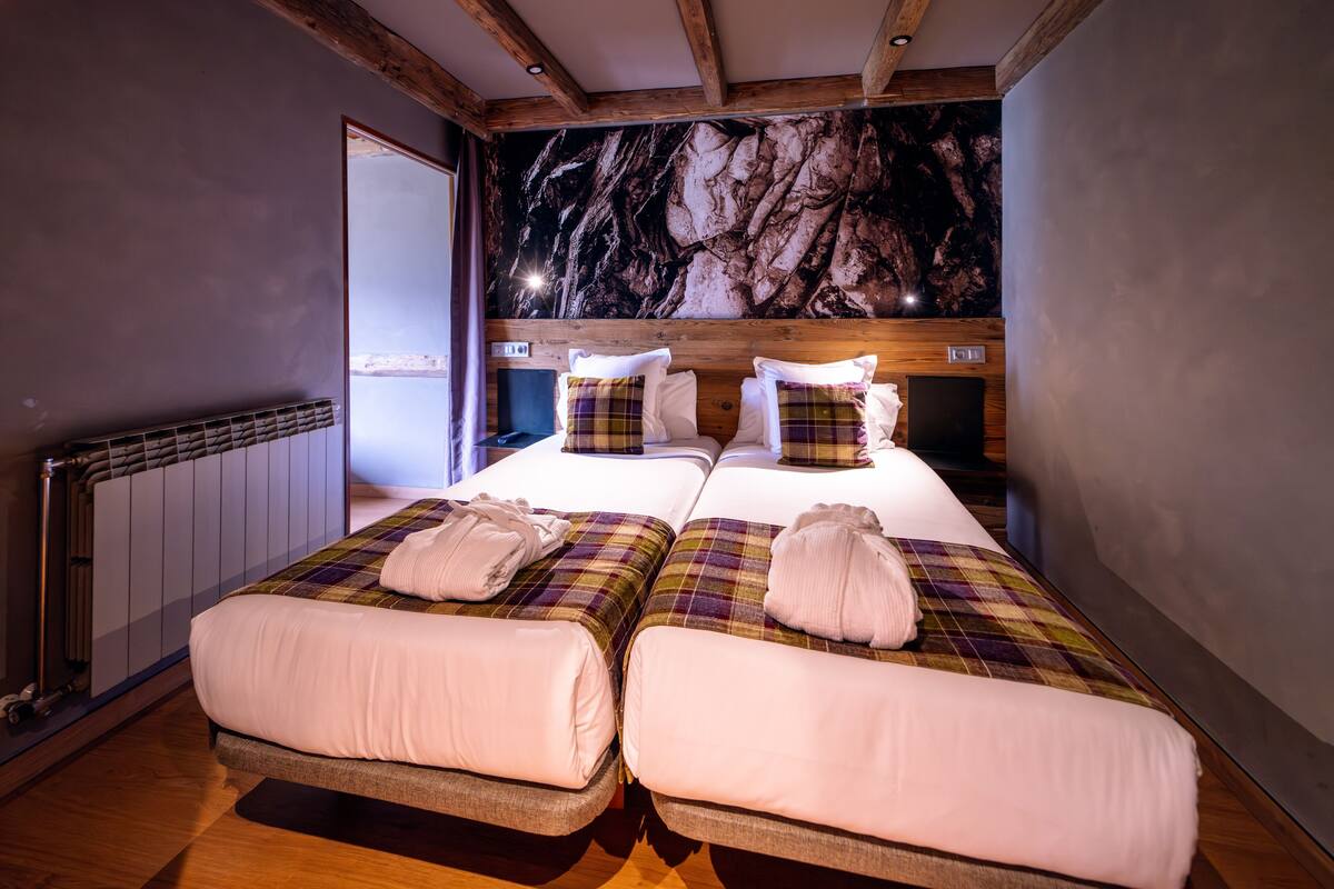 Quarto duplo com duas camas, parede de mármore, vigas de madeira e radiador.