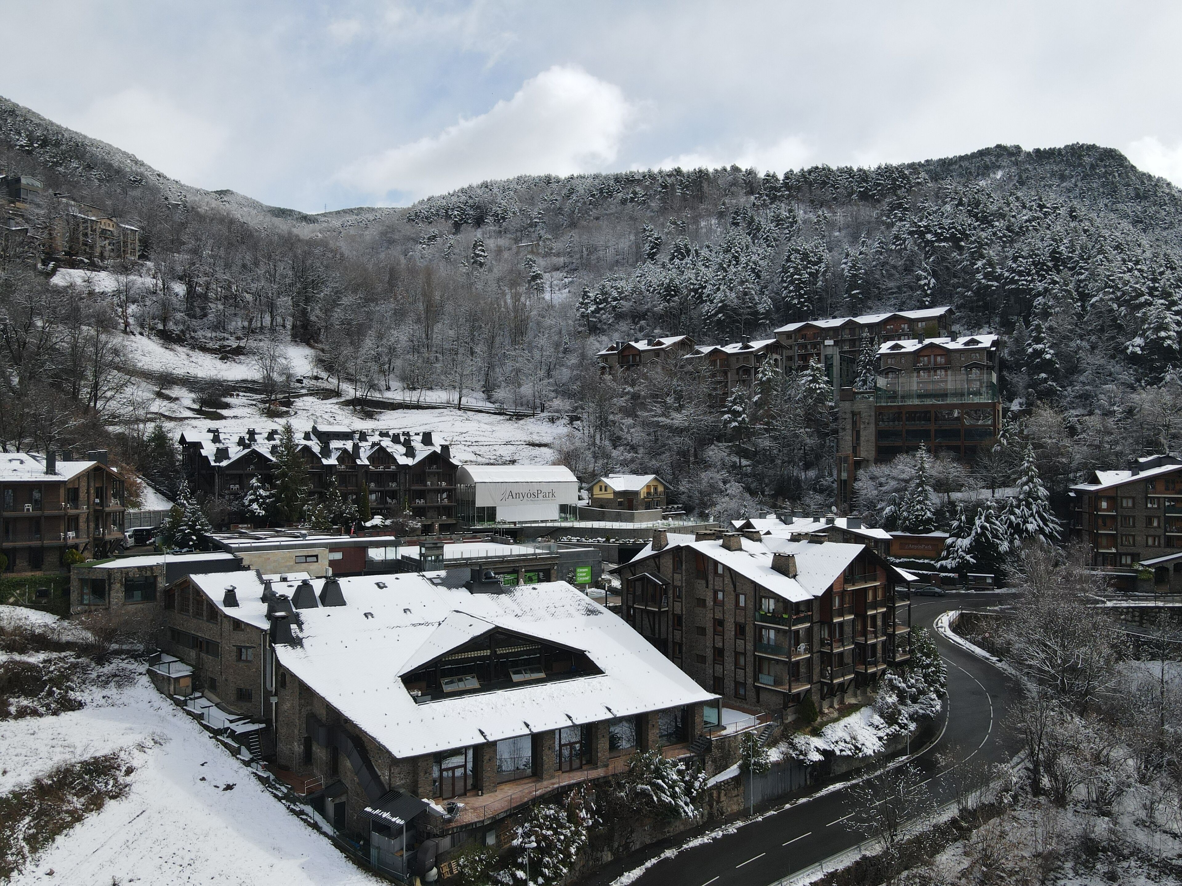 Une station de ski enneigée, avec des bâtiments à l’architecture traditionnelle et moderne, un télésiège et un paysage montagneux en toile de fond.