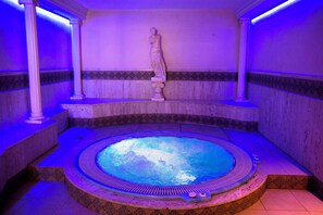 A hot tub with a statue in the center, surrounded by tiled walls and columns.