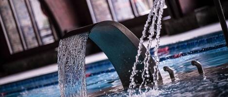 Una fuente con una estructura curva y múltiples chorros de agua en una piscina.