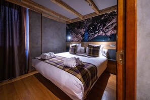 A hotel room with a large bed, wooden ceiling beams, a starry night mural on the wall, and a wooden floor.