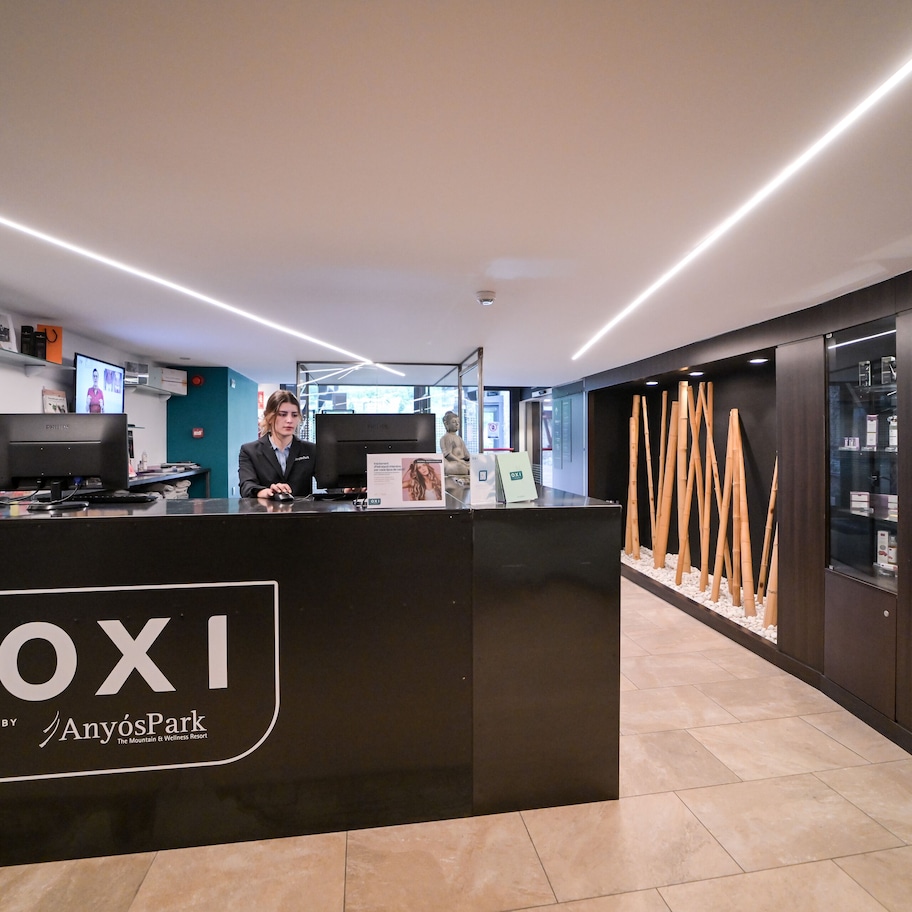 A reception desk with a digital screen, a receptionist, and a display of wooden sticks.