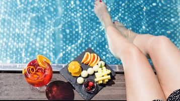 Escena junto a la piscina con una bebida y una bandeja de frutas.