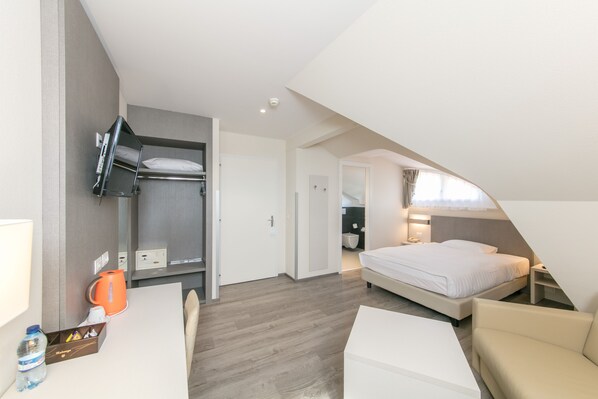 A hotel room with a bunk bed, a desk with a chair, a bedside table, and a small seating area.