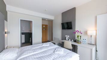 A hotel room with a large bed, a desk with a chair, a TV mounted on the wall, and a small table with a vase of flowers.